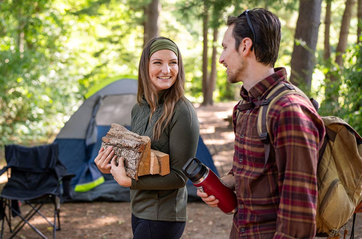 Two people at a forest campsite with a tent and gear.